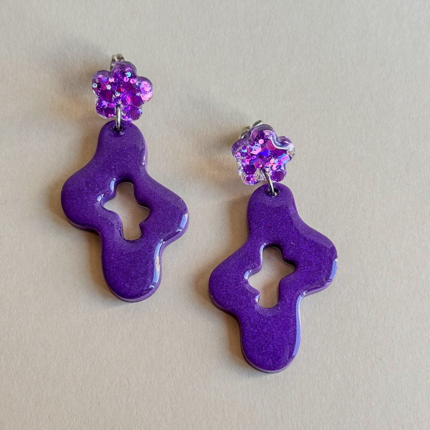 Pendientes hechos a mano de color morado y diseño ondulado con pieza superior en forma de flor pequeña. Hipoalergénicos