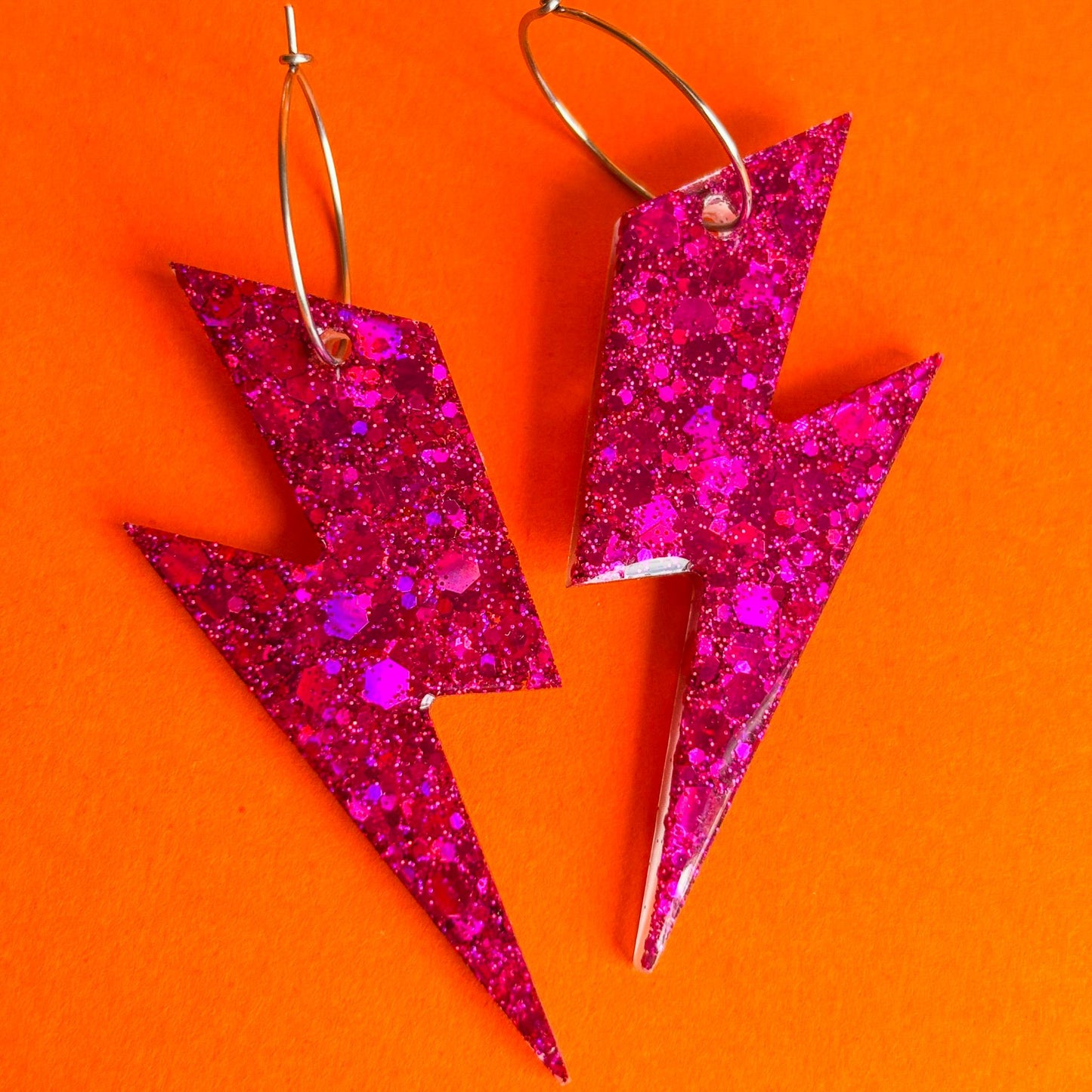 Pendientes de rayos de color rosa fucsia sobre fondo plano color naranja