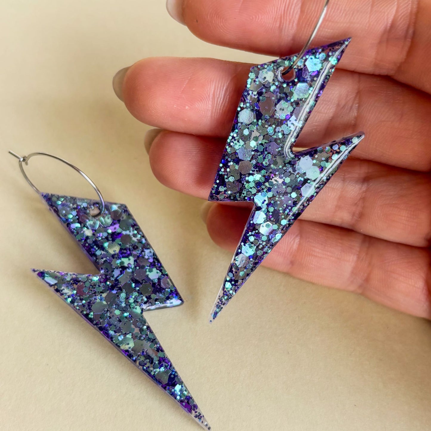 Pendientes de rayos muy brillantes de color lila y azul sobre superficie plana y sobre la mano para que se aprecie bien el color