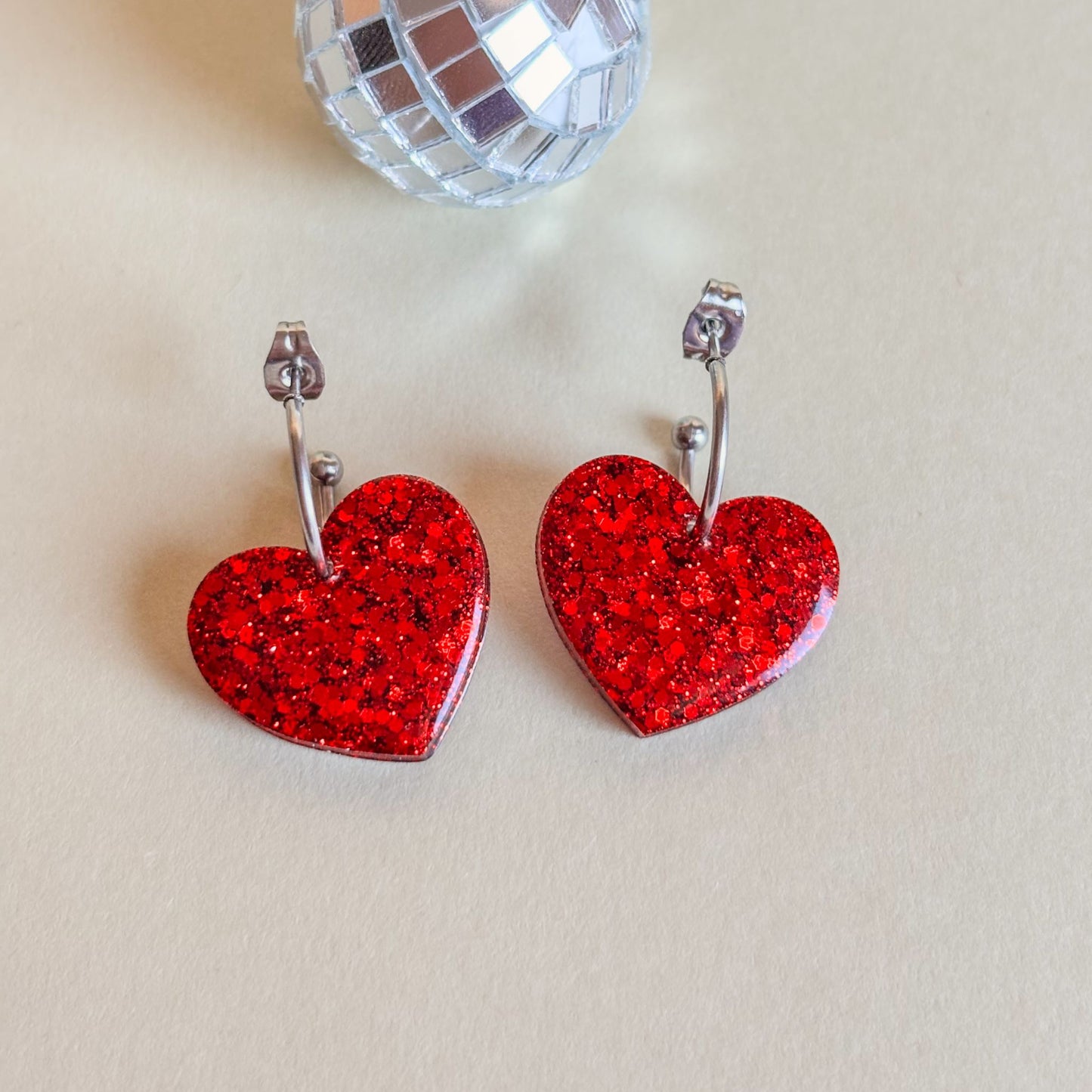 Pendientes de corazones rojos con aros sobre superficie plana.