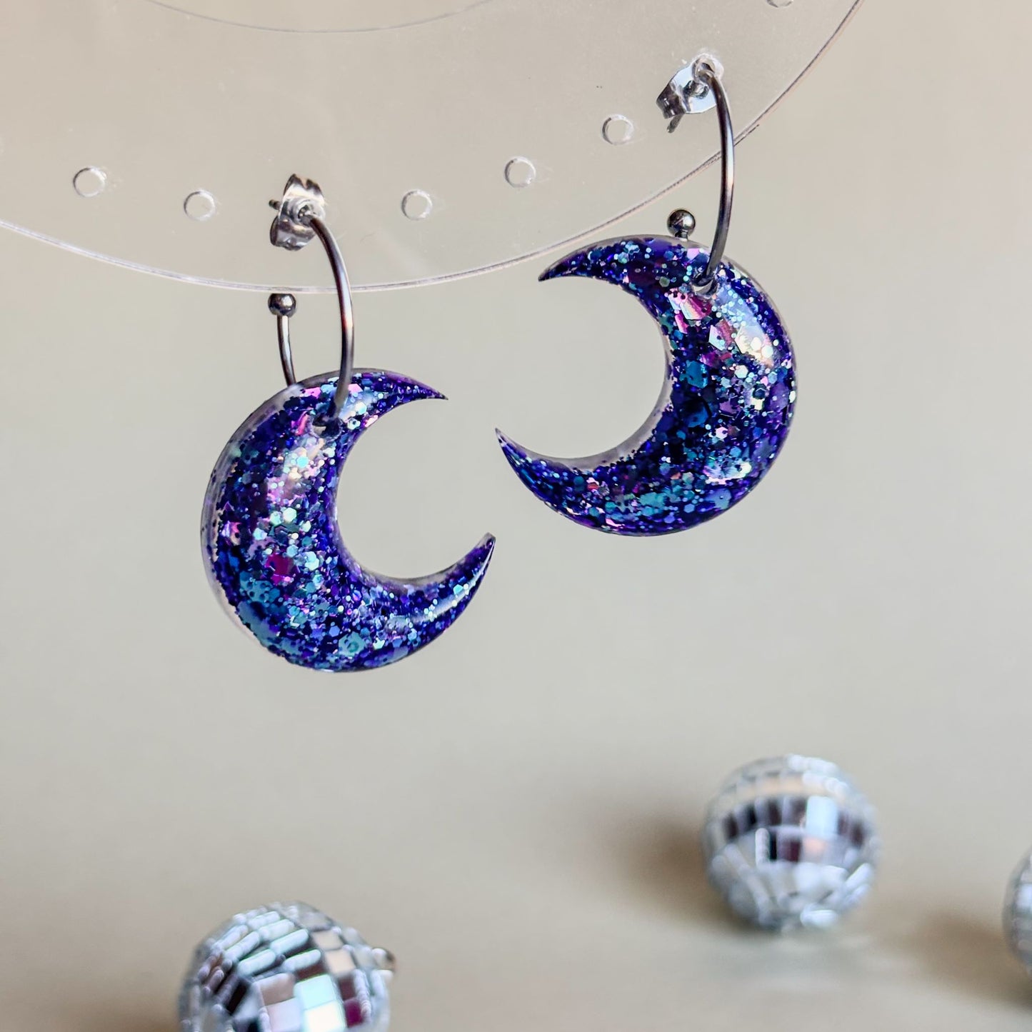 Par de pendientes artesanales en forma de luna con brillo tornasolado de color azul y morado y aros plateados