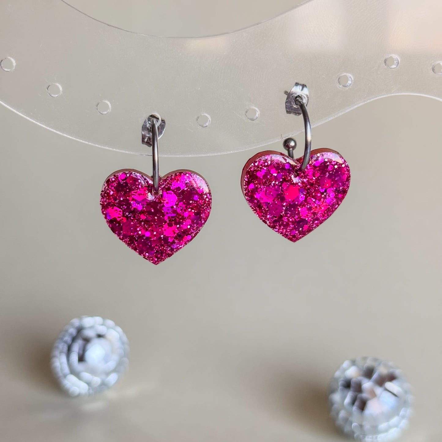 Expositor transparente con pendientes de corazones fucsia hechos a mano.