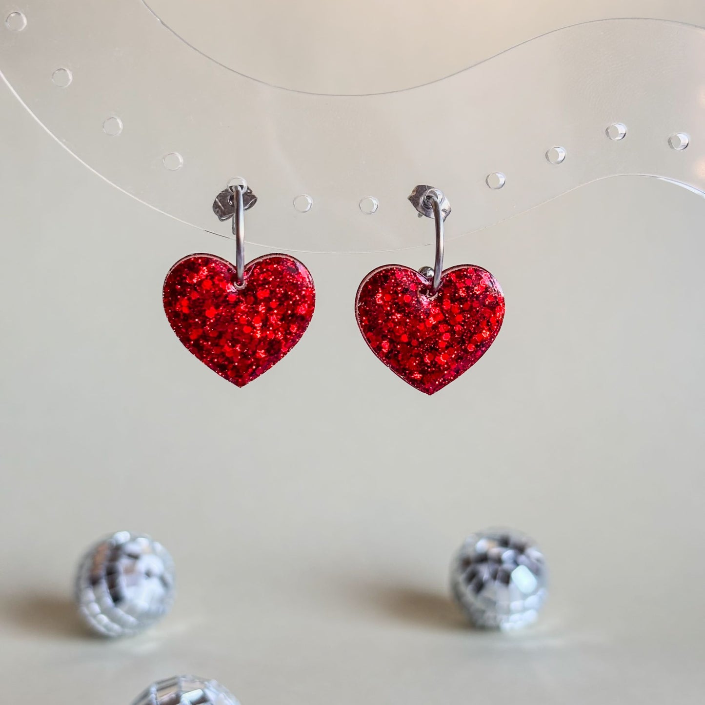 Pendientes de aros de acero inoxidable hipoalergénico con corazones rojos brillantes colgando.