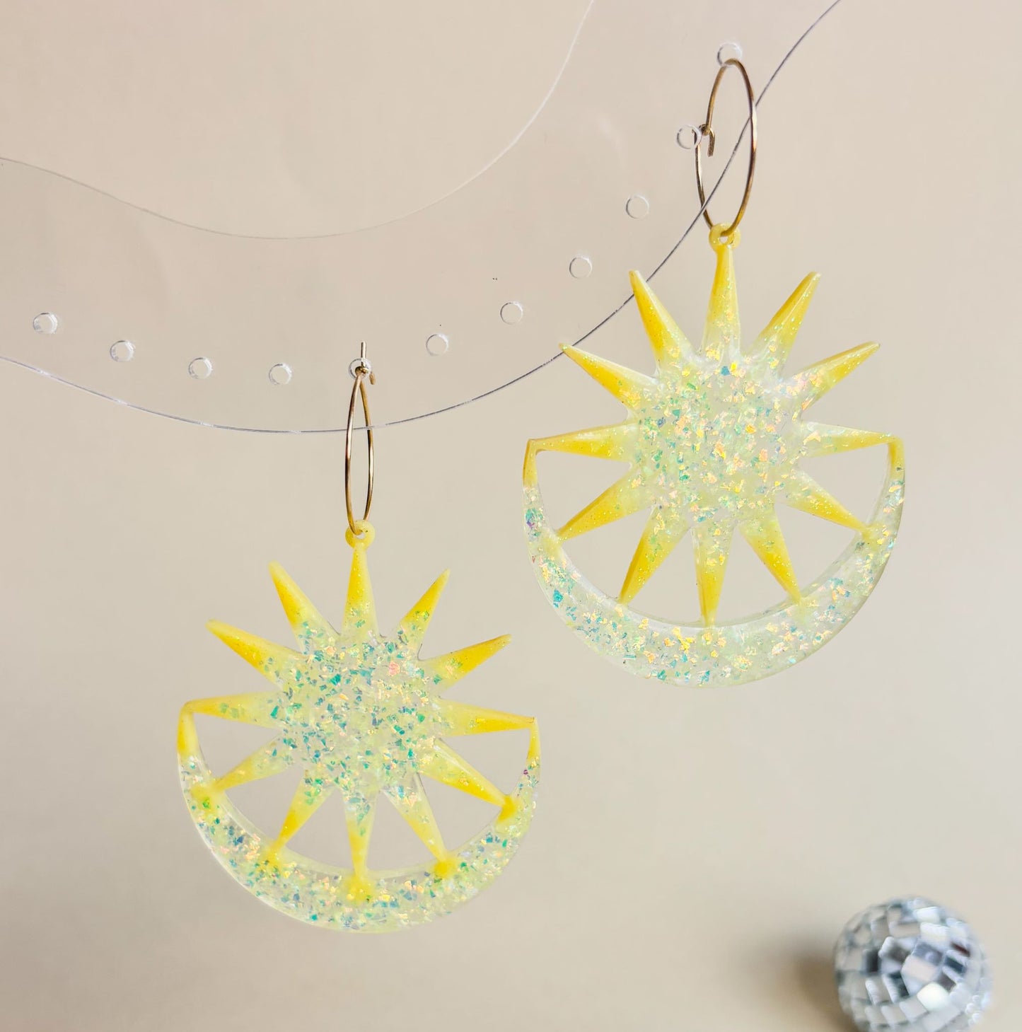 Expositor transparente con preciosos pendientes super vistosos con aros y en forma de sol y luna de color amarillo