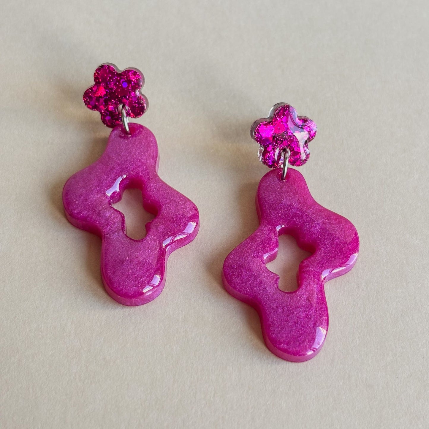 Pendientes artesanales de color rosa precioso con forma ondulada y pequeña flor en la parte superior