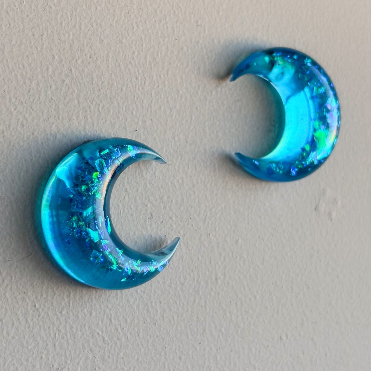 Pendientes translúcidos sobre fondo blanco. Forma de lunas turquesas