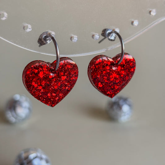 Pendientes de corazones rojos con brillo colgando de expositor transparente
