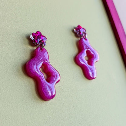 Pendientes de dos piezas, una inferior con forma asimétrica ondulada y una pieza superior pequeña en forma de flor que va pegada al lóbulo de la oreja. Color rosa brillante