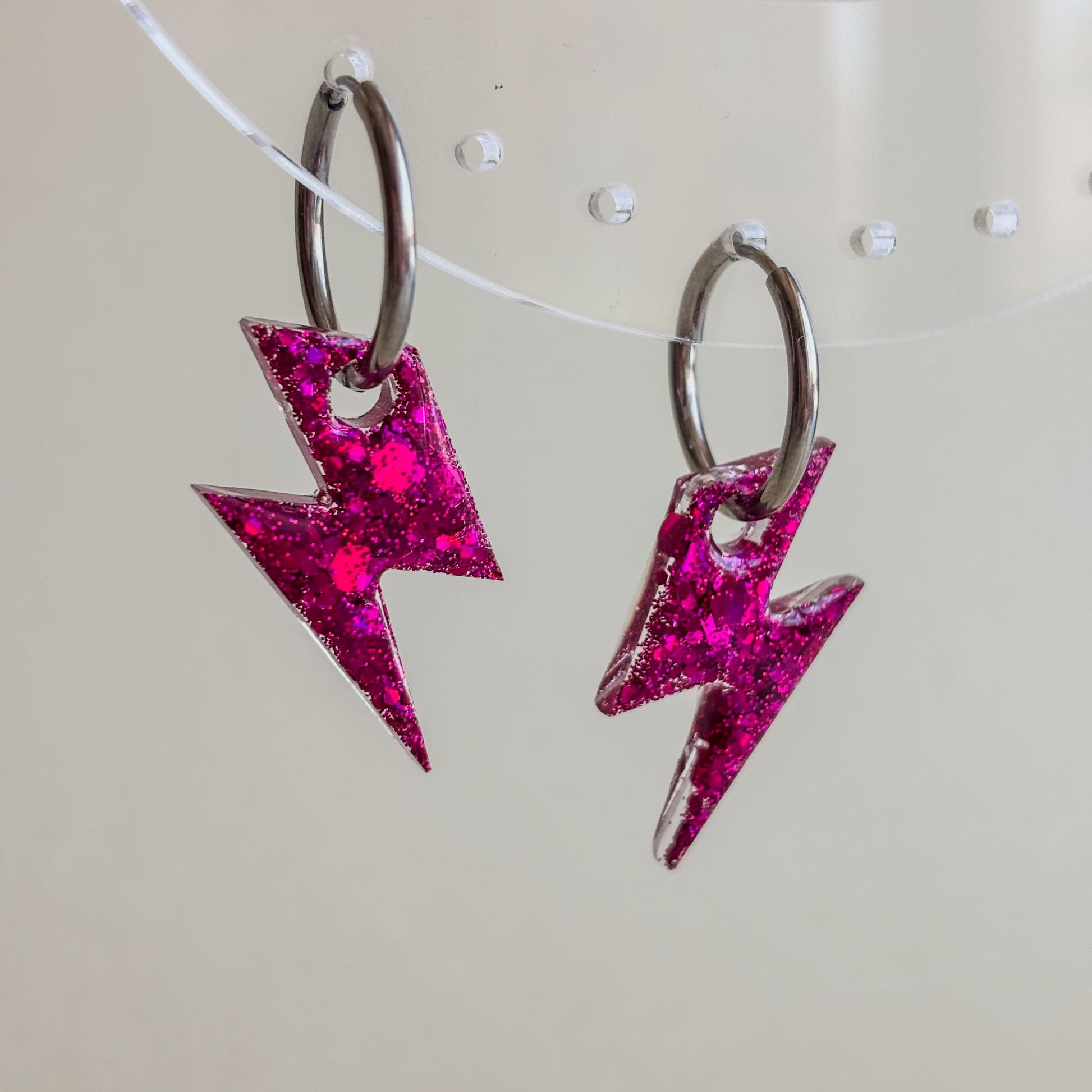 Par de pendientes de rayos pequeños color fucsia muy brillantes con fondo beige, hechos a mano.