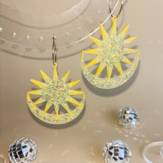 Pendientes en forma de sol y luna, vistosos, grandes y extravagantes, de color amarillo con brillo y aros dorados hipoalergénicos. Foto con luz de frente para que pueda observarse cómo se ve su color según la posición de ésta