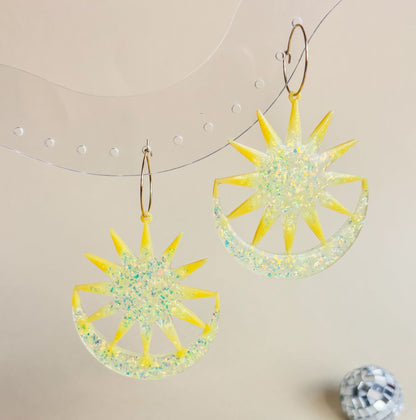 Expositor transparente con preciosos pendientes super vistosos con aros y en forma de sol y luna de color amarillo