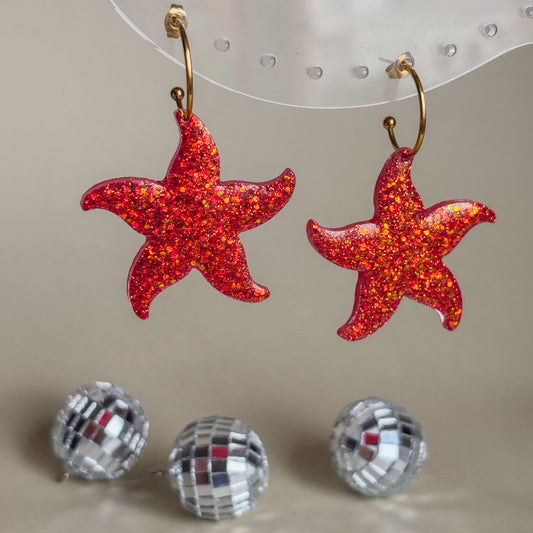 Pendientes de estrellas de mar rojas con brillo anaranjado y aros dorados. Hechos a mano con resina epoxi